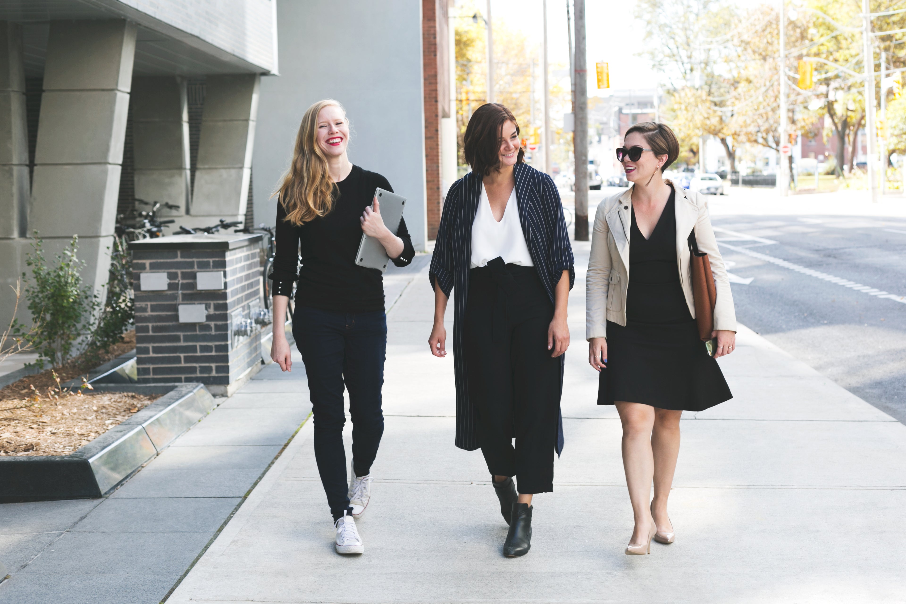 three woman walking on city sidewalk.