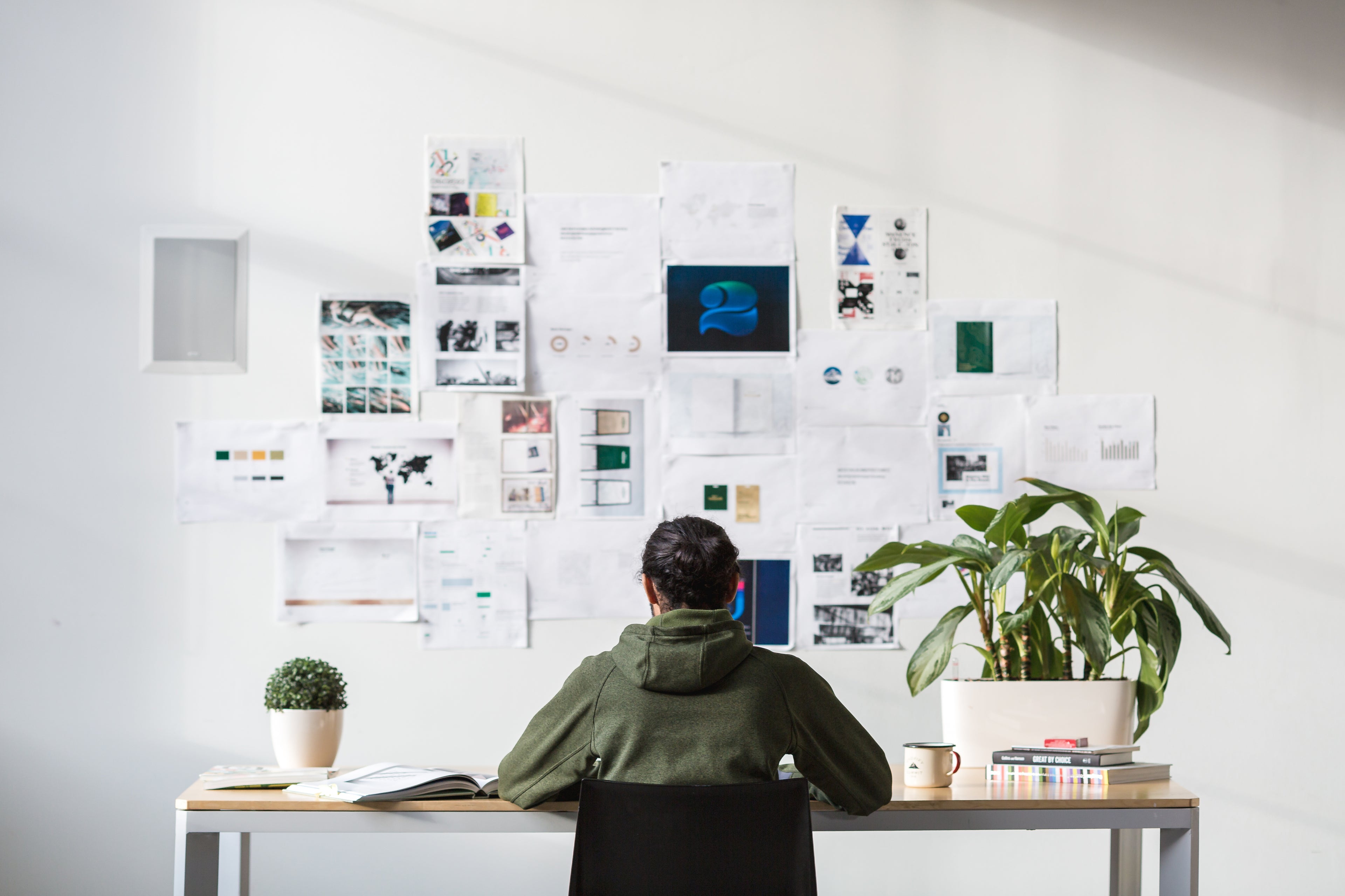 person working at desk with a collage of design inspiration taped on the wall 